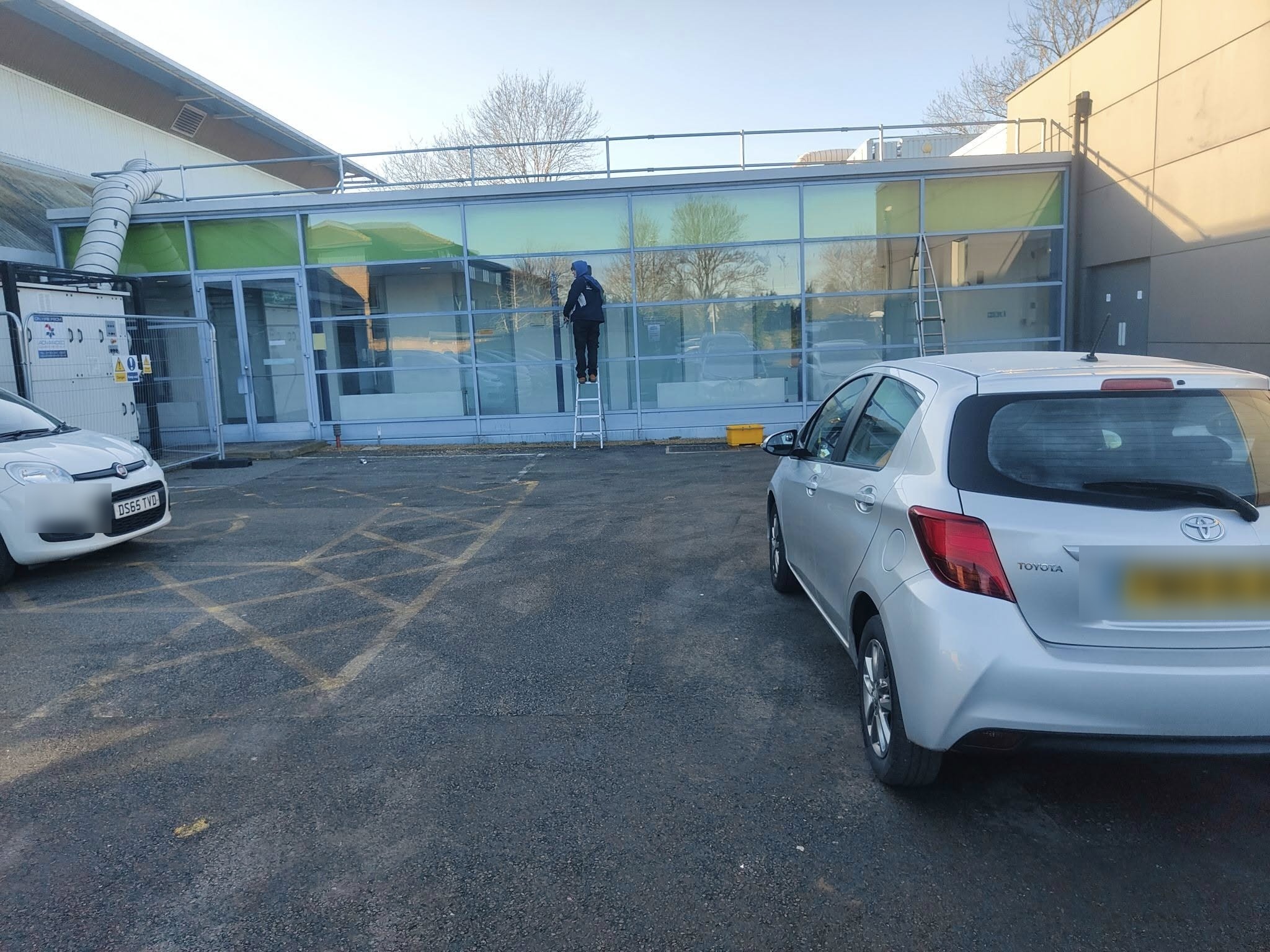 Window cleaner on a ladder at the long glass front of a leisure centre