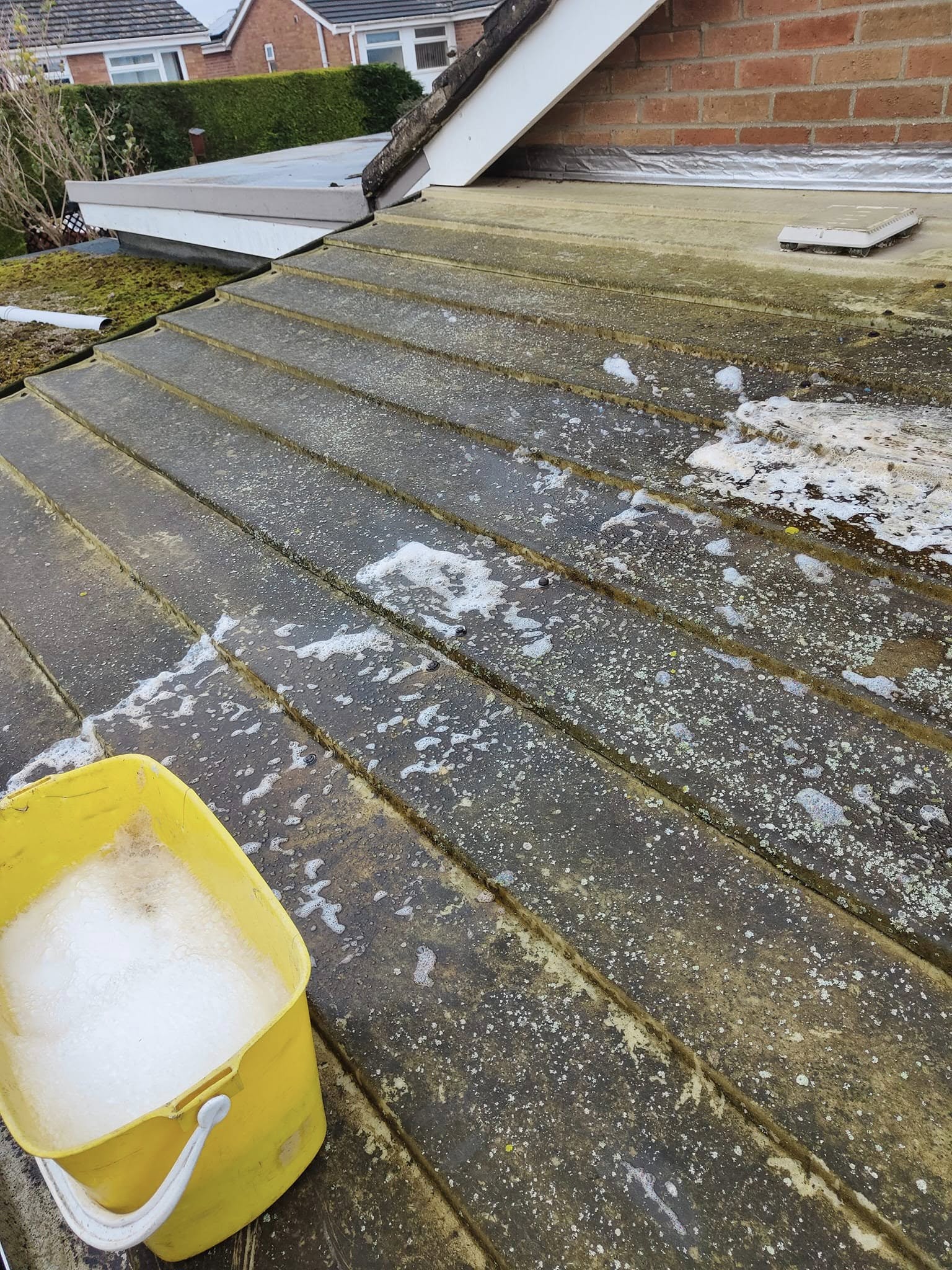 Conservatory roof covered in grime with a bucket of cleaning foam