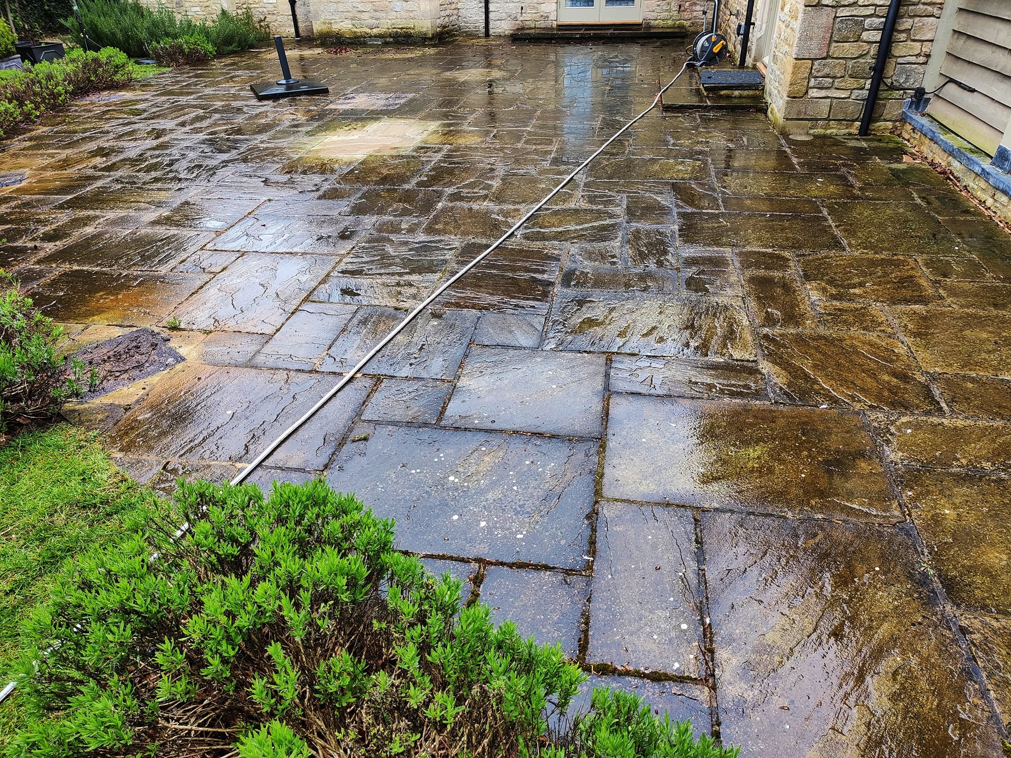 Stone patio wet mid-clean with the jet wash lance on the slabs