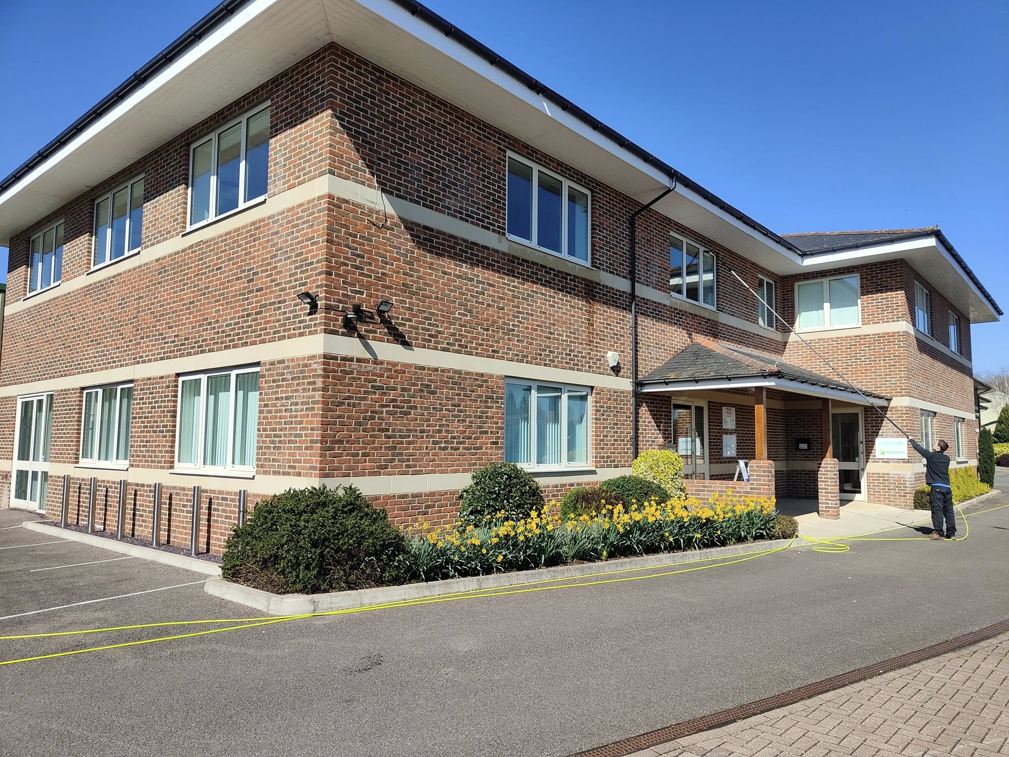 Two-storey brick office block with flower beds, a window cleaner at the entrance