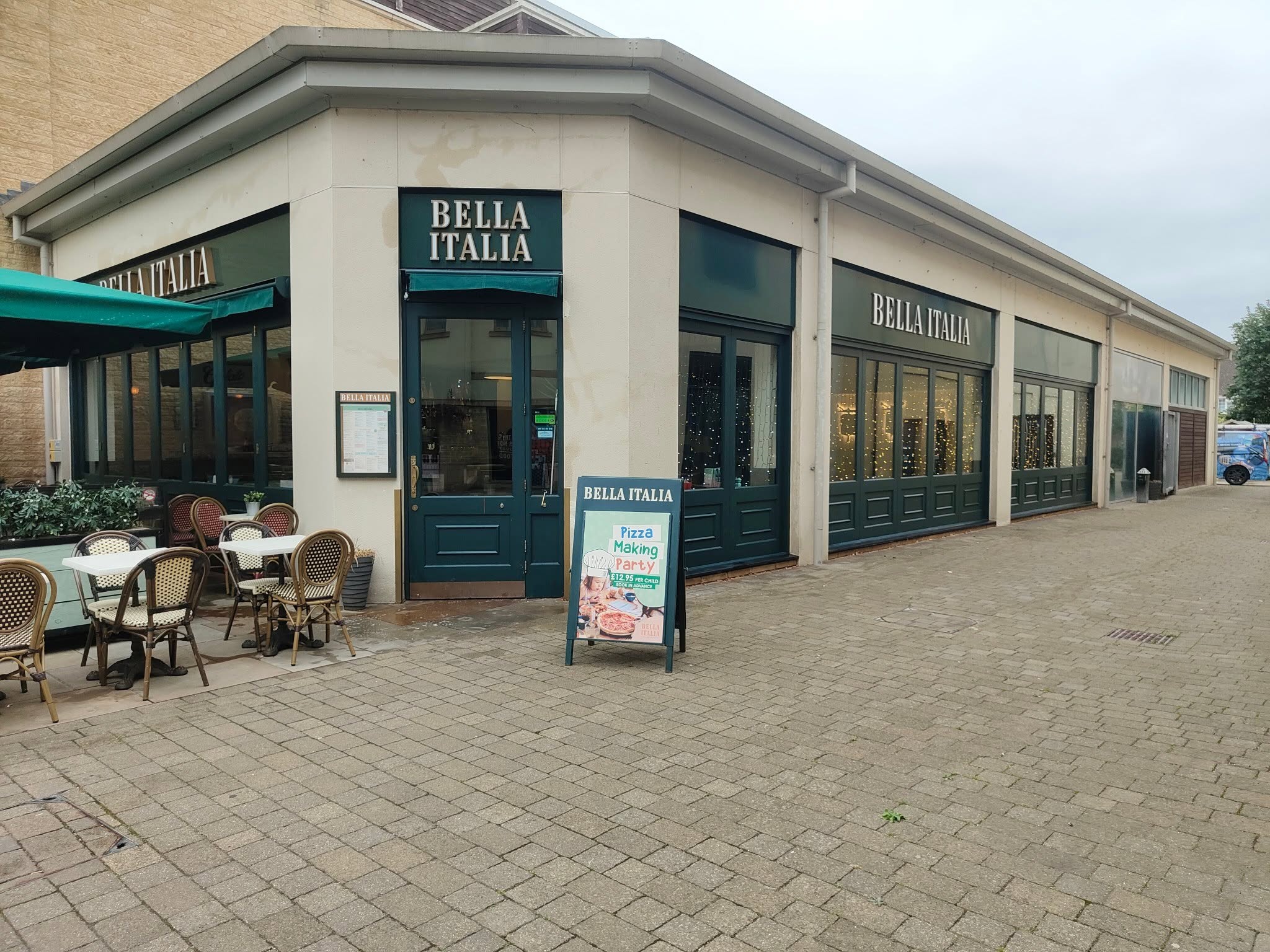 Clean restaurant frontage with dark green shopfronts and tables outside