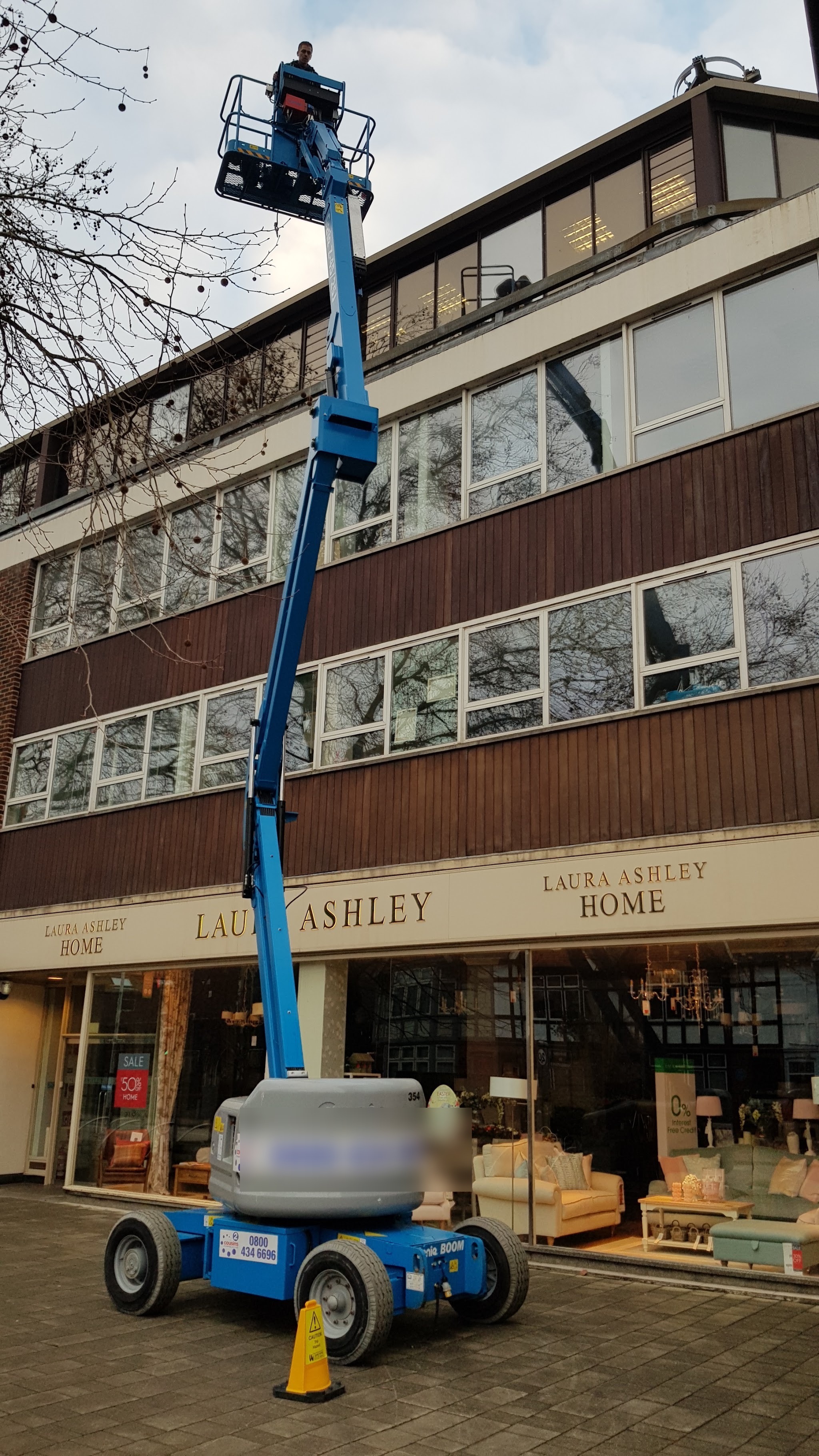 Cleaner in a cherry picker basket at the upper windows above a high street shop